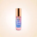 A body mist bottle with pump by Swiss Miss, labeled 'Vanilla Charm', featuring a metallic rose gold cap and a body of liquid with a vertical rainbow gradient of pink, purple, blue, and green, set against a soft beige background.