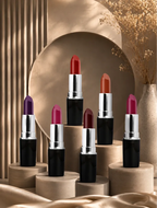 Six open Swiss Miss Classic Lipsticks featuring Ruby Romance and other shades displayed on beige pedestals against an arched backdrop.