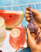 Hand holding Swiss Miss Maple Sugar 831 Get Set Go quick dry nail enamel bottle displaying sophisticated muted brownish-mauve polish applied on long nails.
