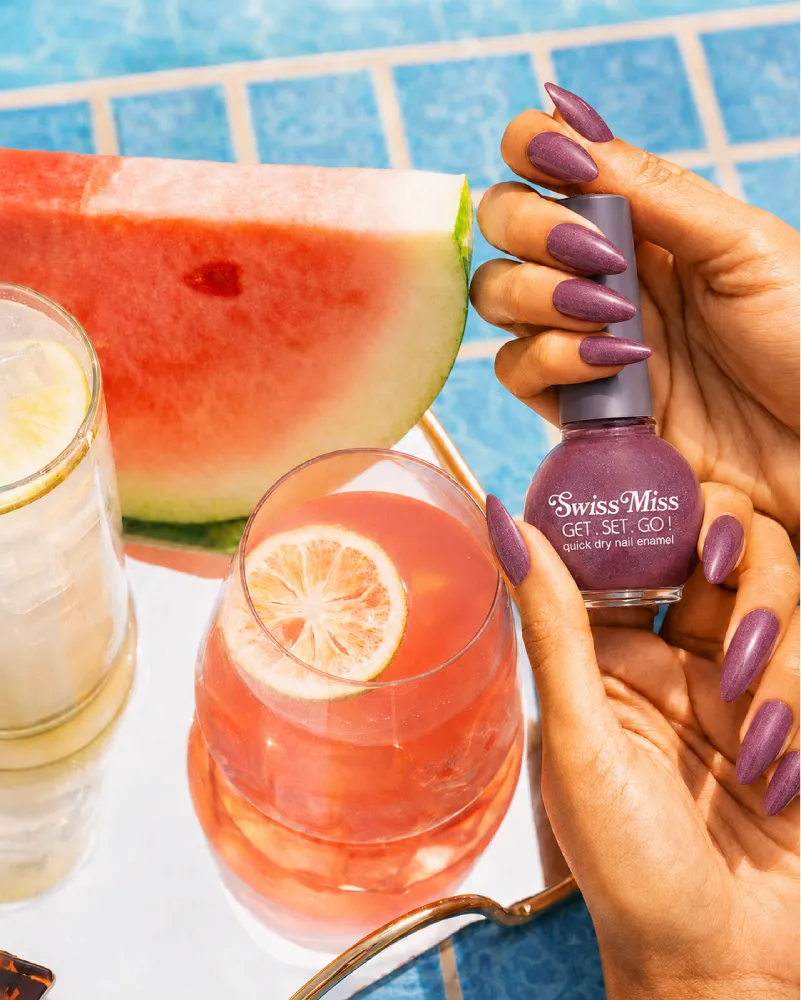 Hand holding Swiss Miss Pink Carnation 822 Get Set Go quick dry nail enamel bottle displaying shimmering dusty rose pink polish applied on long nails.