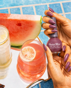 Hand holding Swiss Miss Pink Carnation 822 Get Set Go quick dry nail enamel bottle displaying shimmering dusty rose pink polish applied on long nails.