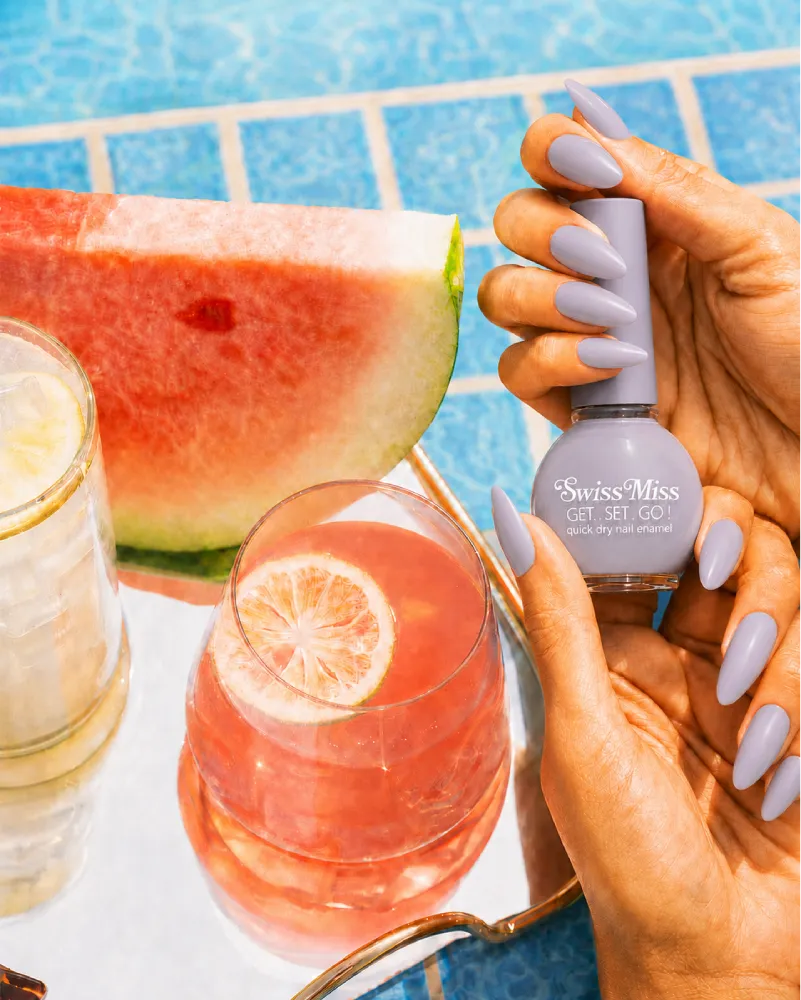 Hand holding Swiss Miss White Pearl 807 Get Set Go quick dry nail enamel bottle displaying iridescent silvery white pearl polish applied on long nails.