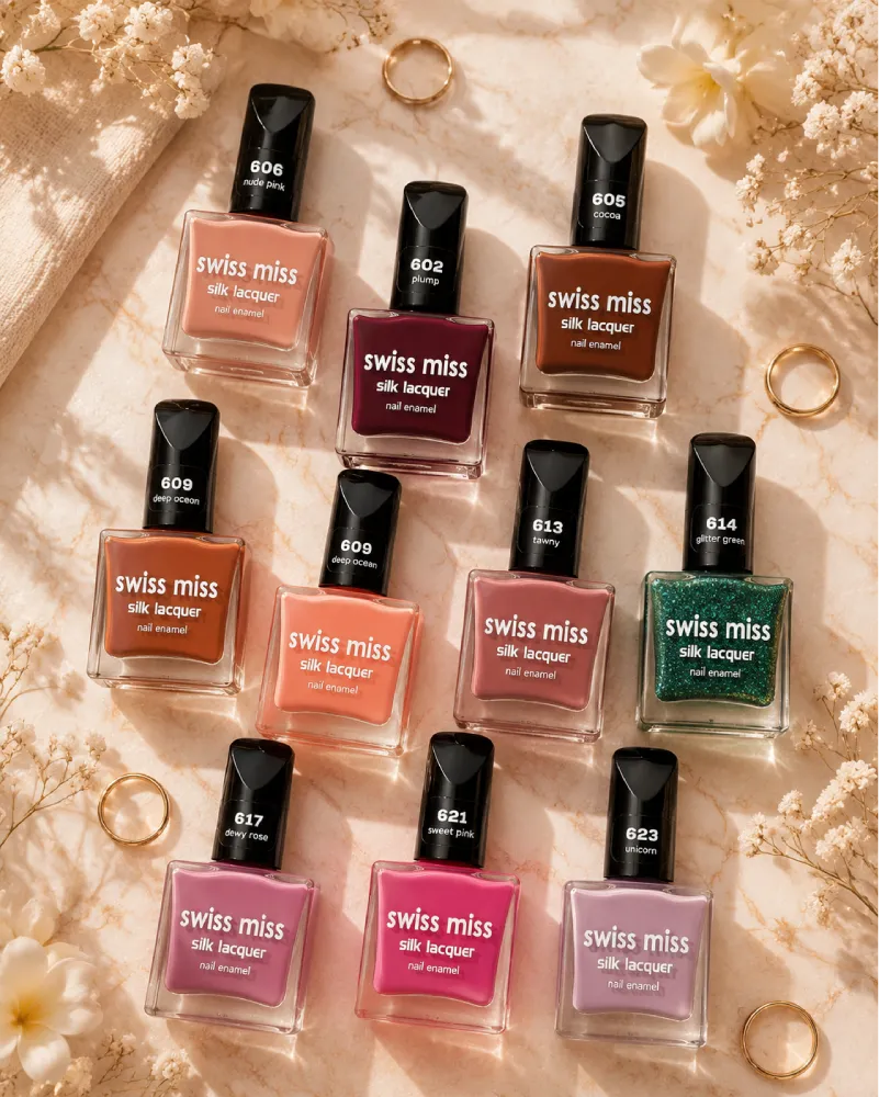 Top-down aesthetic flat lay of various Swiss Miss Silk Lacquer nail polish bottles displayed on a beige marble surface with white flowers and gold rings.